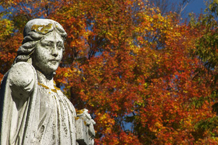 A weathered statue of a maiden with bright fall foliage
